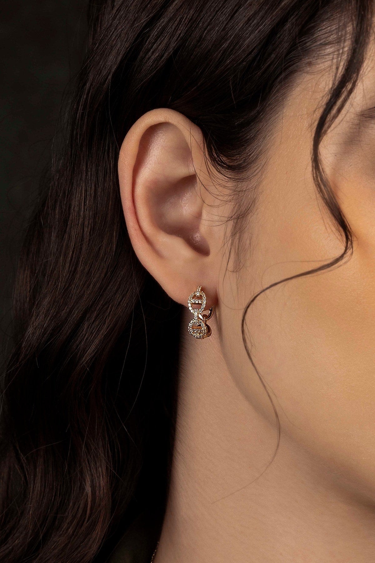 Close-up of an ear wearing a gold earring with a dark background