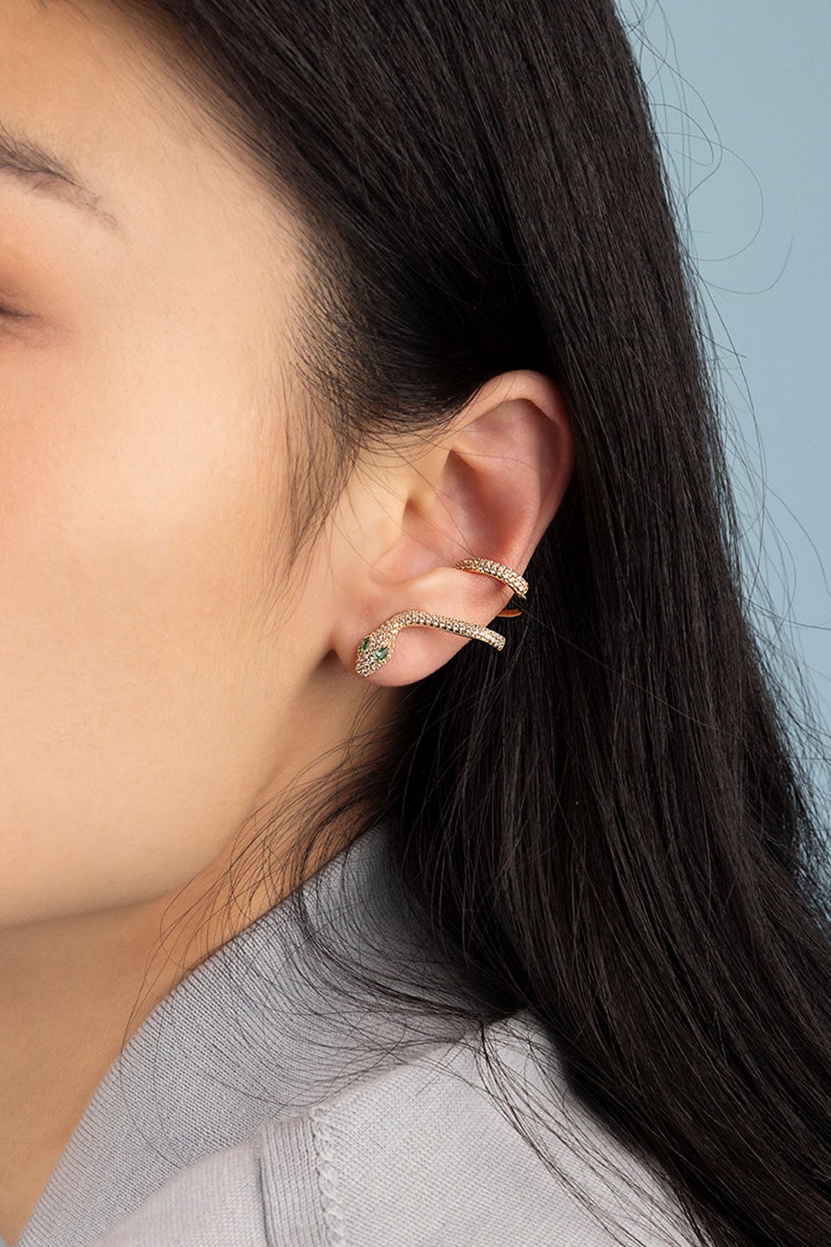 Close-up of a person wearing gold hoop earrings with a neutral background